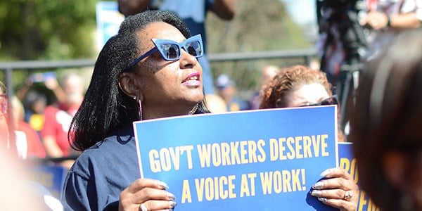 Black woman holding sign at a rally that says Gov't Workers Deserve A Voice at Work!