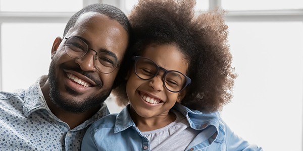 Black family smiling at the camera. Both people are wearing glasses. 