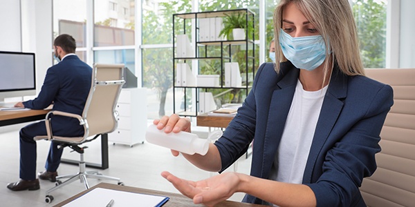 Worker putting on hand sanitizer and wearing a mask